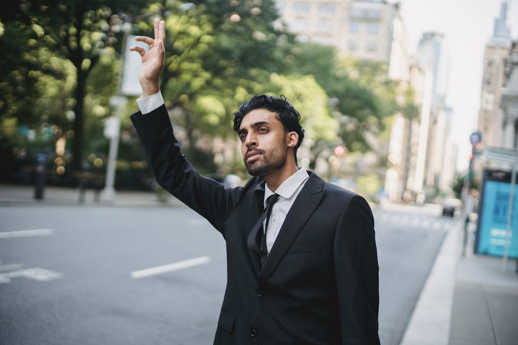 A man in a suit raises his hand to hail a taxi on a city street.